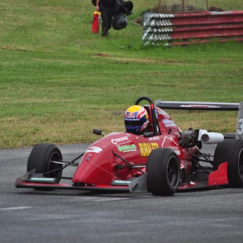 编辑郑一鸣站在贴满换算公式便签的墙前讲解美金人民币汇率换算思路的全身照，画面偏暗调带颗粒感